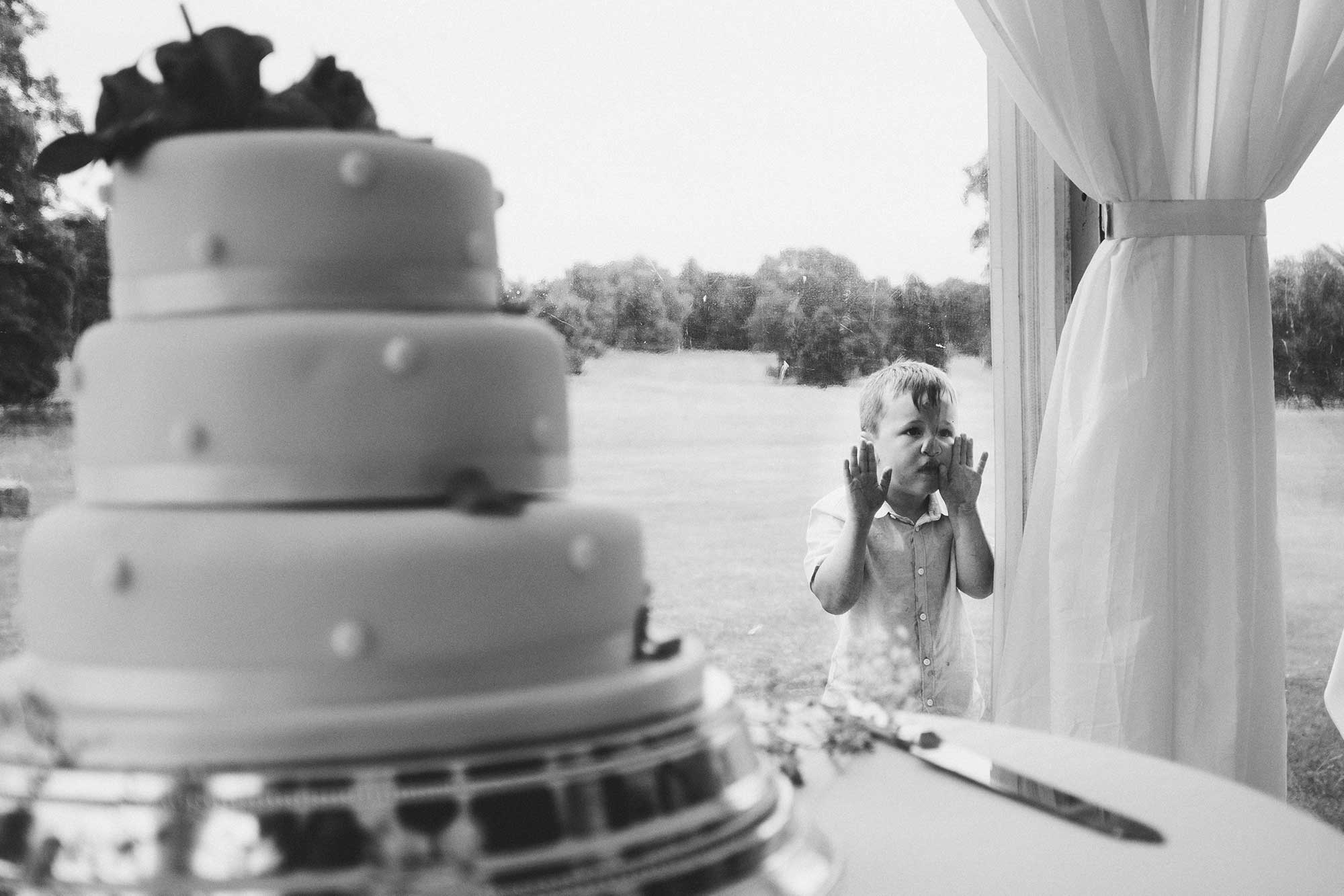 boy presses face against glass looking at wedding cake