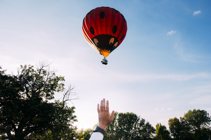 hot air balloon flies over wedding and guest waves